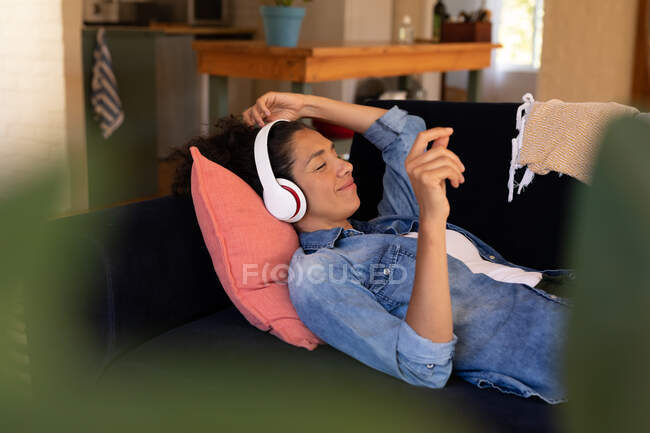 Kaukasische Frau auf Sofa liegend, Kopfhörer aufgesetzt, zu Hause entspannt. Zu Hause bleiben in Selbstisolierung während Quarantäne Lockdown. — Stockfoto