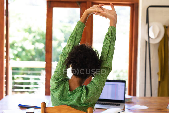 Вид ззаду кавказької жінки, що сидить за столом, використовуючи ноутбук комп'ютер, що розтягує руки в повітрі. перебування вдома в самоізоляції під час карантину . — стокове фото