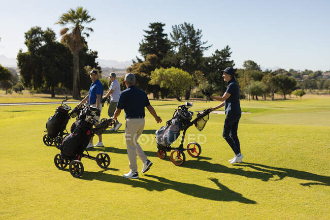 Vier kaukasische Senioren gehen mit Golftaschen über den Golfplatz. Golf-Sport-Hobby, gesunder Lebensstil im Ruhestand — Stockfoto