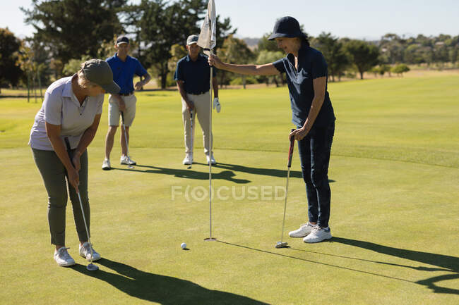 Hommes et femmes âgés caucasiens regardant la femme prendre le tir sur le vert. golf passe-temps sportif, mode de vie sain à la retraite — Photo de stock