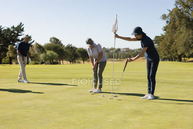 Blanc senior homme et femme regardant homme prenant le tir sur le vert. Golf passe-temps sportif, mode de vie sain à la retraite — Photo de stock