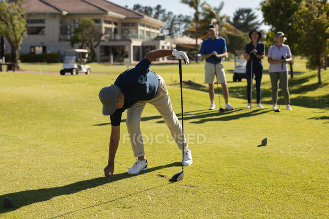Tres hombres y mujeres mayores caucásicos observando a un hombre preparándose para un disparo en el green. deportes de golf hobby, estilo de vida de jubilación saludable - foto de stock