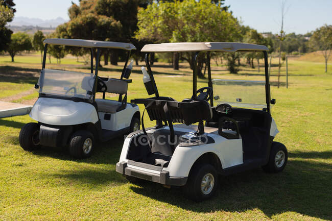 Два гольф-баггі, що стоять на полі для гольфу в сонячний день. гольф спортивне хобі, здоровий спосіб життя на пенсії . — стокове фото