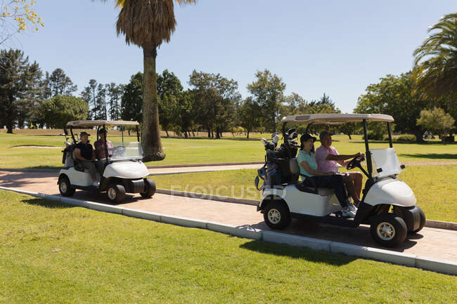 Dos parejas mayores caucásicas conduciendo buggy de golf en el campo de golf hablando y sonriendo. deportes de golf hobby, estilo de vida de jubilación saludable. - foto de stock