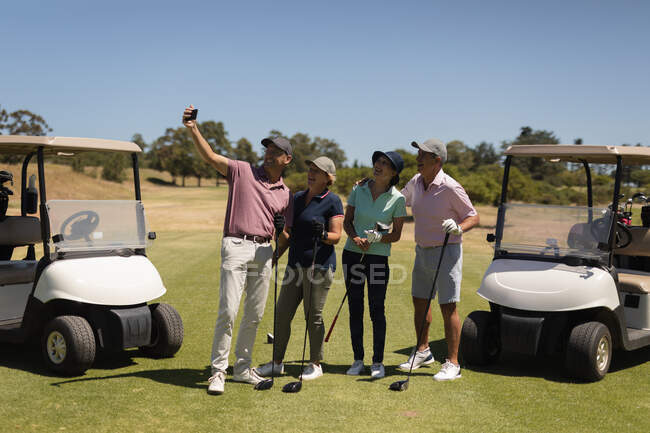 Cuatro hombres y mujeres mayores caucásicos sosteniendo palos de golf y tomando una selfie. Golf deportes hobby, estilo de vida de jubilación saludable - foto de stock