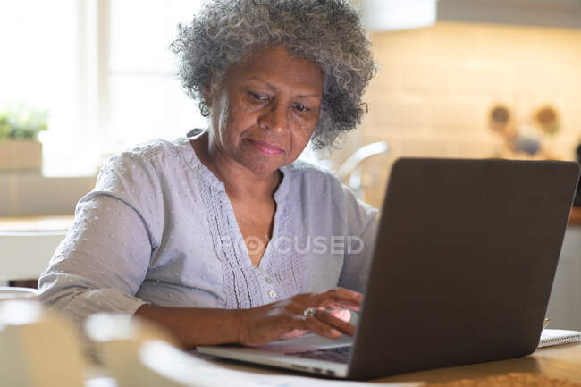 Pensativo afroamericano anciano mujer usando el ordenador portátil en casa. permaneciendo en casa en aislamiento en cuarentena - foto de stock