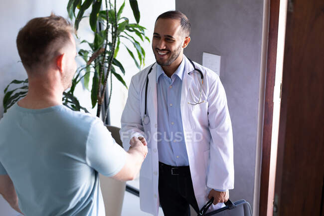 Mixed race male doctor greeting male patient at home. hygiene healthcare protection during coronavirus covid 19 pandemic. — Stock Photo