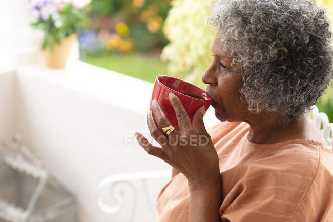 Considerável afro-americana idosa bebendo café enquanto estava sentada no alpendre da casa. permanecer em auto-isolamento em quarentena — Fotografia de Stock