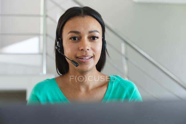 African american woman wearing phone headset having a video call on laptop at home. staying at home in self isolation in quarantine lockdown — Stock Photo