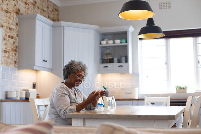 Thoughtful african american senior woman holding empty medication containers at home. staying at home in self isolation in quarantine lockdown — Stock Photo