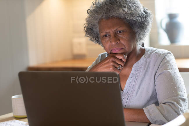 Продумана афроамериканська старша жінка, яка використовує ноутбук вдома. перебування вдома в самоізоляції в карантині — стокове фото