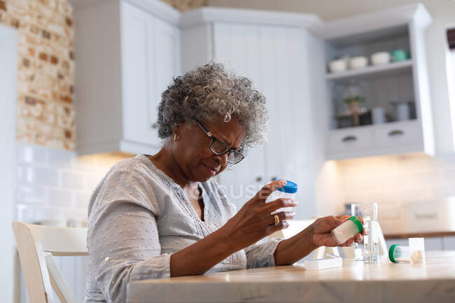 Thoughtful african american senior woman holding empty medication containers at home. staying at home in self isolation in quarantine lockdown — Stock Photo