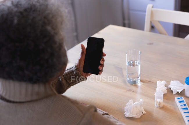 Rückansicht einer afrikanisch-amerikanischen Seniorin, die ihr Smartphone zu Hause benutzt. Zu Hause bleiben in Selbstisolierung in Quarantäne — Stockfoto
