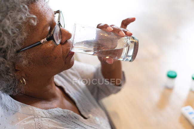 Nahaufnahme einer nachdenklichen afrikanisch-amerikanischen Seniorin, die zu Hause Wasser trinkt. Zu Hause bleiben in Selbstisolierung in Quarantäne — Stockfoto