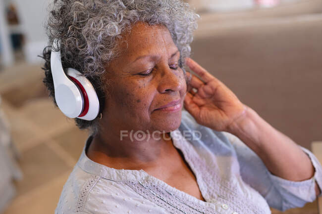 Afro-americana idosa usando fones de ouvido gostando de ouvir música em casa. ficar em casa em auto-isolamento em quarentena — Fotografia de Stock