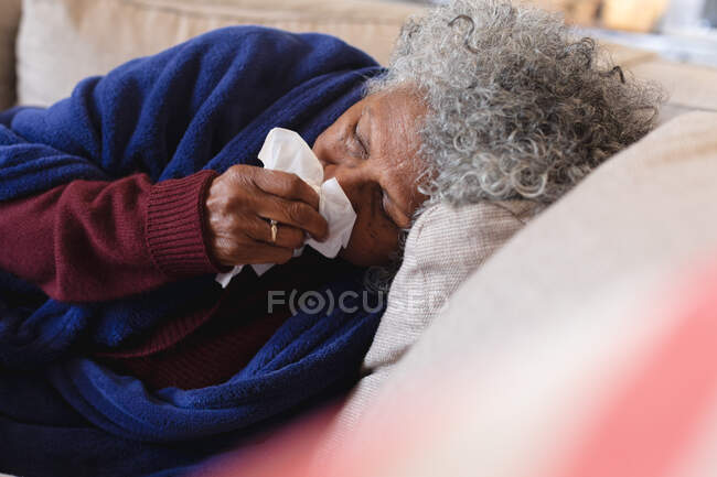 Sick african american senior woman lying on the couch. staying at home in self isolation in quarantine lockdown — Stock Photo