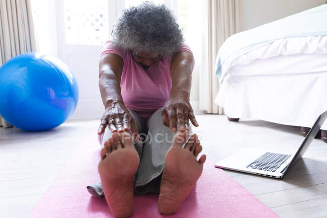 Африканская старшая женщина, практикующая йогу дома. оставаться дома в изоляции в карантинной изоляции — стоковое фото
