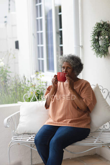 Nachdenkliche afrikanisch-amerikanische Seniorin mit Kaffeetasse auf der Veranda des Hauses sitzend. Isolation in Quarantäne — Stockfoto