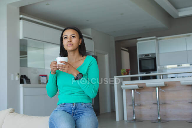 Afroamerikanerin trinkt Kaffee, während sie zu Hause auf der Couch sitzt. Zu Hause bleiben in Selbstisolierung in Quarantäne — Stockfoto