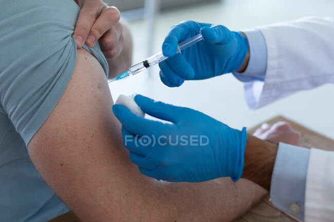 Врач смешанной расы в маске для лица делает прививку пациенту мужского пола. защита гигиены здравоохранения во время пандемии коронавируса. — стоковое фото