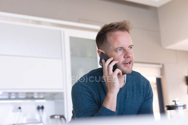 Hombre caucásico hablando usando smartphone en casa. permanecer en casa en aislamiento durante el bloqueo de cuarentena. - foto de stock