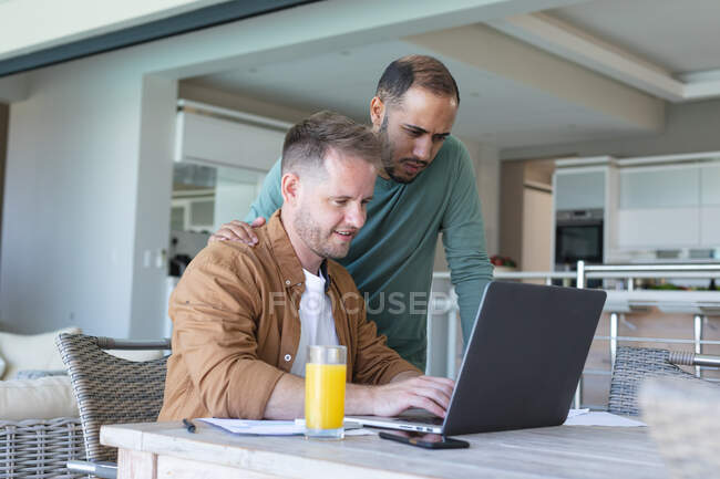 Multi ethnic gay male couple going through bills and using laptop at home. staying at home in self isolation during quarantine lockdown. — Stock Photo
