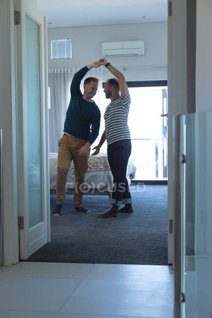 Couple homosexuel multi ethnique dansant dans un salon à la maison. Rester à la maison en isolement personnel pendant le confinement en quarantaine. — Photo de stock