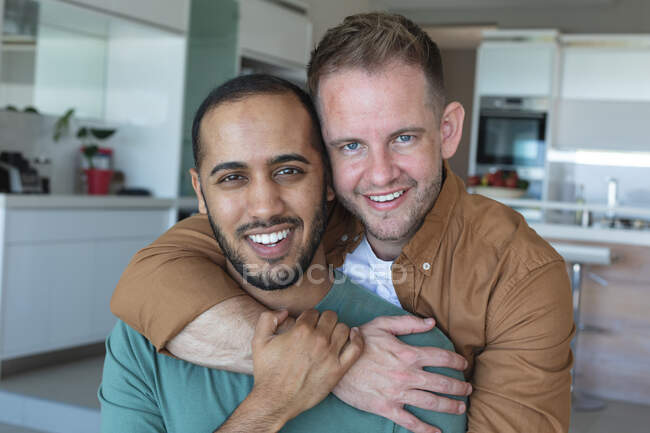 Multi etnico gay maschio coppia abbracciare guardando la fotocamera e sorridendo a casa. stare a casa in isolamento durante l'isolamento in quarantena. — Foto stock