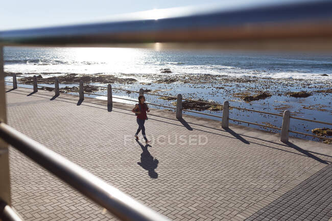 Happy african american woman wearing backpack walking on promenade by the sea. Digital nomad on the go lifestyle. — Stock Photo