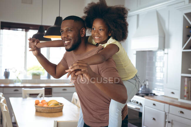 Afroamerikaner und seine Tochter huckepack in der Küche. Während der Quarantäne zu Hause bleiben und sich selbst isolieren. — Stockfoto