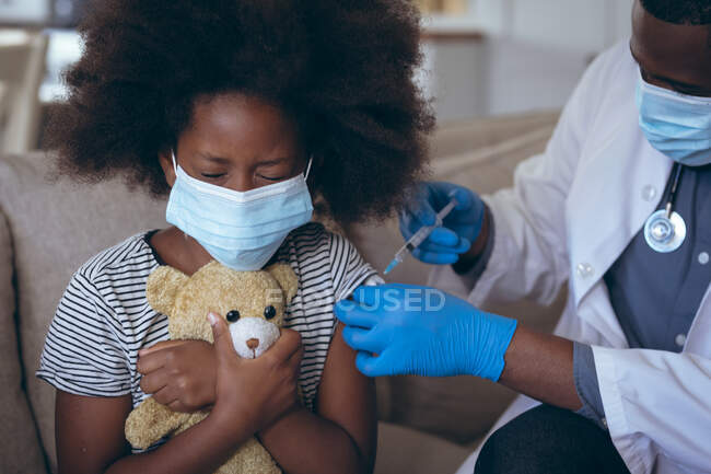 Médico afroamericano vacunando a su hijo paciente. permanecer en casa en aislamiento durante el bloqueo de cuarentena. - foto de stock
