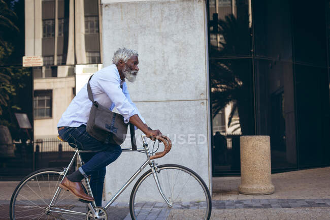 African american senior man riding bicycle in the street past doorway. digital nomad out and about in the city. — Stock Photo
