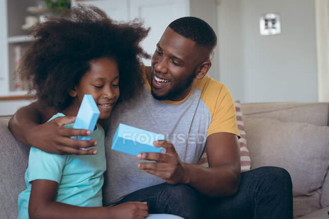 Afroamerikanerin sitzt im Wohnzimmer und schenkt ihrem Vater ein Geschenk. Während der Quarantäne zu Hause bleiben und sich selbst isolieren. — Stockfoto