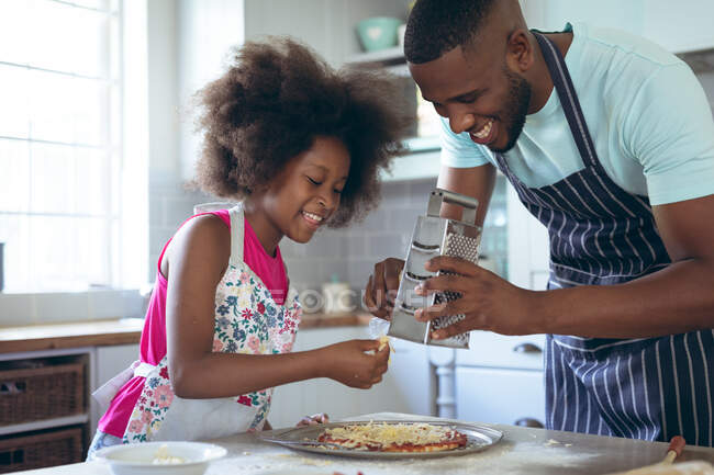 Fille afro-américaine et son père font une pizza ensemble dans la cuisine. rester à la maison en isolement personnel pendant le confinement en quarantaine. — Photo de stock