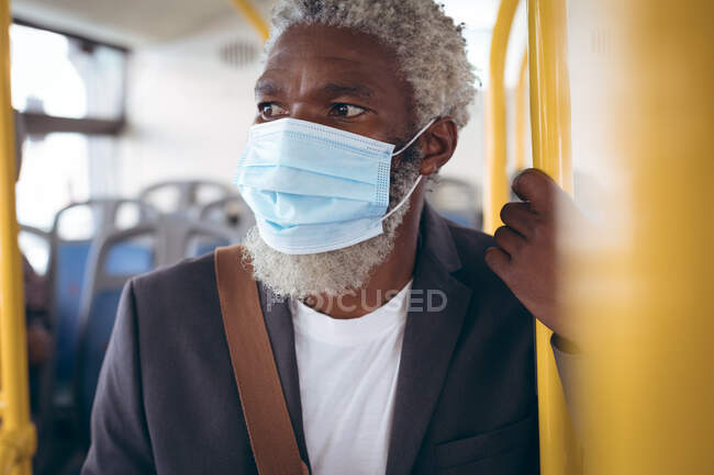 Старший африканский американец в маске, стоящий в автобусе. Цифровой кочевник в городе во время пандемии коронавируса. — стоковое фото