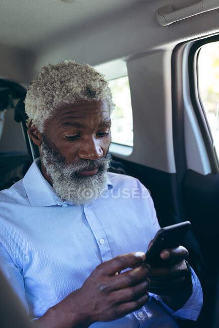 Hombre mayor afroamericano sentado en taxi usando smartphone. nómada digital en la ciudad. - foto de stock