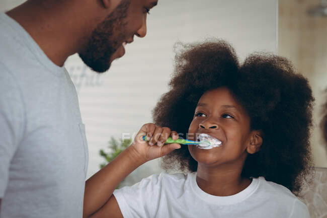 African american girl and her father brushing teeth together. staying at home in self isolation during quarantine lockdown. — Stock Photo