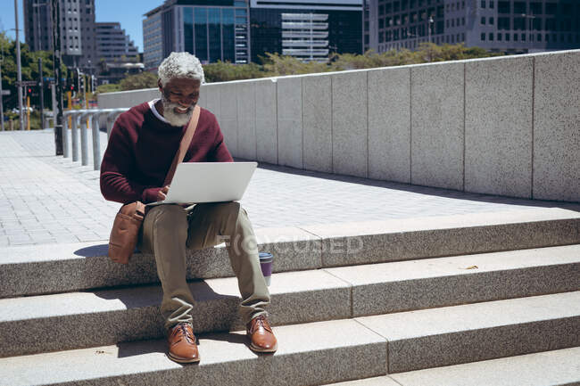 Ein afroamerikanischer Senior sitzt mit Laptop auf der Straße. digitaler Nomade in der Stadt unterwegs. — Stockfoto