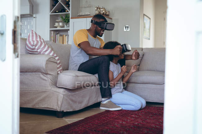 Homme afro-américain et sa fille assis dans le salon en utilisant un casque vr. rester à la maison en isolement personnel pendant le confinement en quarantaine. — Photo de stock
