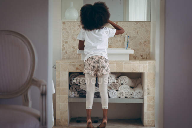 Chica afroamericana de pie en el baño cepillándose los dientes. permanecer en casa en aislamiento durante el bloqueo de cuarentena. - foto de stock