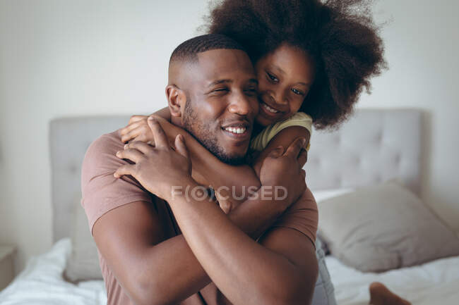 Hombre afroamericano y su hija abrazándose en la cama. permanecer en casa en aislamiento durante el bloqueo de cuarentena. - foto de stock