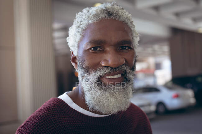Porträt eines lässig gekleideten afrikanisch-amerikanischen Seniors mit Bart, der auf der Straße lächelt. digitaler Nomade in der Stadt unterwegs. — Stockfoto