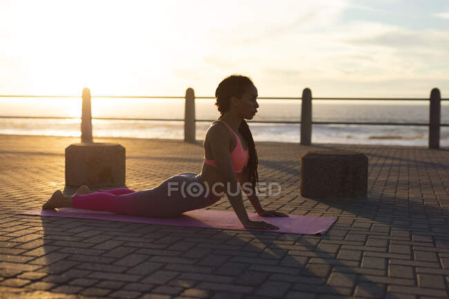 African american woman exercising on promenade by the sea doing yoga. fitness healthy outdoor lifestyle. — Stock Photo
