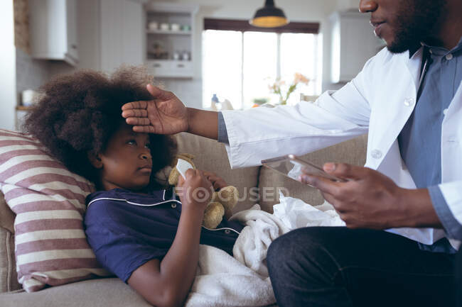 Médico afroamericano comprobando la temperatura del paciente infantil. permanecer en casa en aislamiento durante el bloqueo de cuarentena. - foto de stock