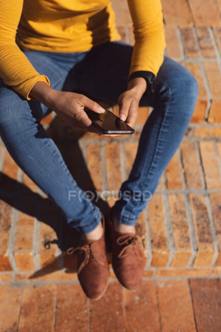 Midsection of woman sitting using smartphone on promenade by the sea. Digital nomad on the go lifestyle. — Stock Photo