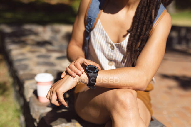 Midsection of african american woman sitting using her smartwatch in park. Digital nomad on the go lifestyle. — Stock Photo