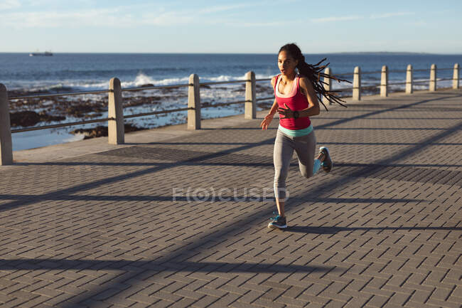 Afroamerikanerin beim Joggen auf einer Strandpromenade. Fitness und gesunder Lebensstil im Freien. — Stockfoto