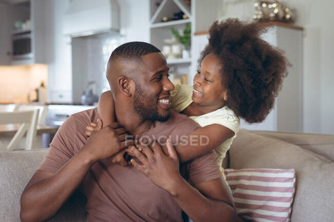L'uomo afroamericano e sua figlia abbracciati sul divano. stare a casa in isolamento durante l'isolamento in quarantena. — Foto stock