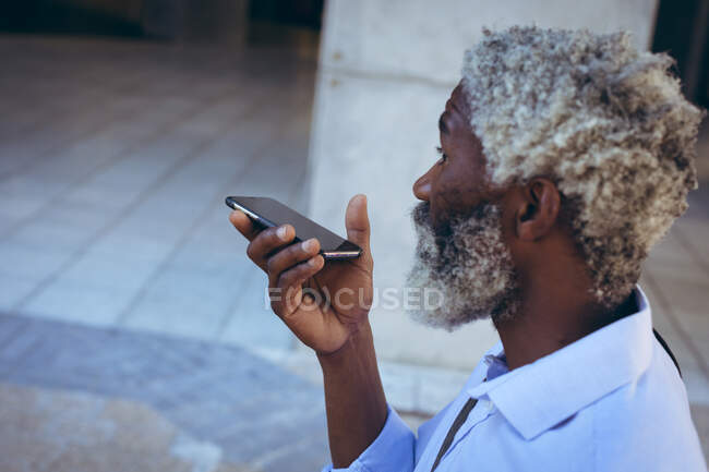 Afro-americano idoso em pé na rua falando no smartphone. nômade digital para fora e sobre na cidade. — Fotografia de Stock