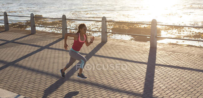 Eine Afroamerikanerin, die sich auf einer Strandpromenade beim Laufen konzentriert. Fitness und gesunder Lebensstil im Freien. — Stockfoto